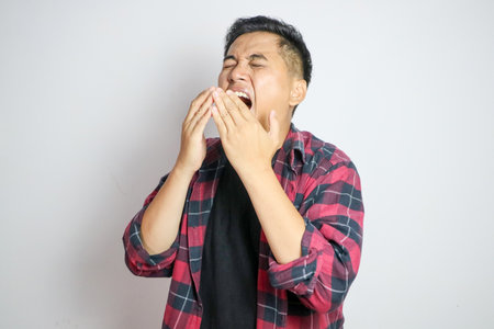 A Southeast Asian man sneezing while holding his nose. Captures a moment of discomfort, suitable for themes related to health, allergies, or cold symptoms in various marketing or editorial contextsの写真素材