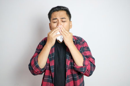 Adult Asian man cover his nose and mouth with tissue when sneezingの写真素材