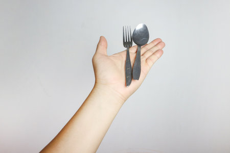 A hand holding a spoon and fork. Isolated in white background. Side view.の写真素材
