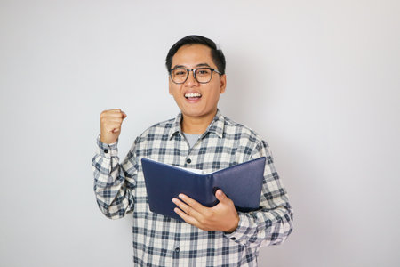 Adult Asian man showing excited gesture with fist clenched when reading a bookの写真素材