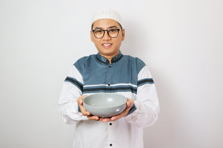 Happy asian muslim man standing while offering food concept. Man holds a bowl. Isolated on white backgroundの写真素材