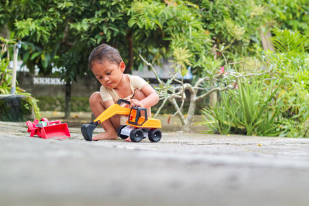 Children holding yellow excavator vehicle toy outdoorの写真素材