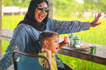 Happy Muslim mother and child enjoying the natural atmosphere with traditional Indonesian food and drinksの写真素材