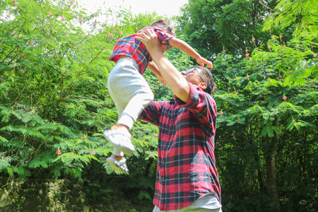 Asian father lifting son into the air while playing together in the parkの写真素材