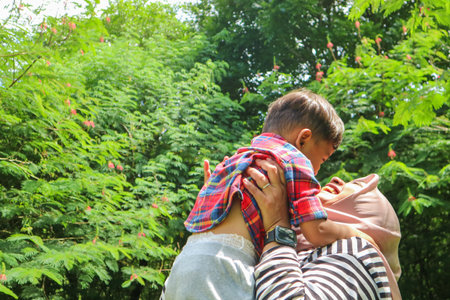 Mother in hijab happily holding her baby outdoors, surrounded by lush greenery, capturing tender moments of love and bonding in natureの写真素材