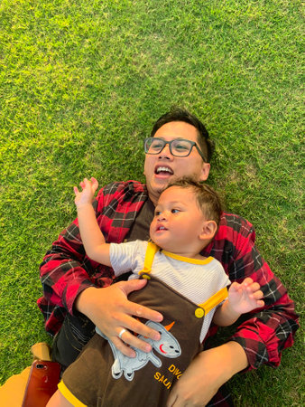Boy lying on father. Father lying on green grass outside.の写真素材