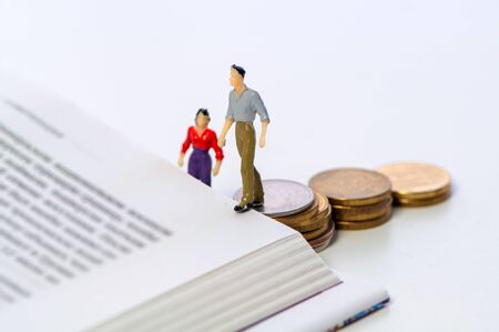 Miniature couple walking up coins onto a bookの写真素材