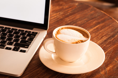Hot latte coffee cup in a white cup on a table laptob in coffee shop.の写真素材