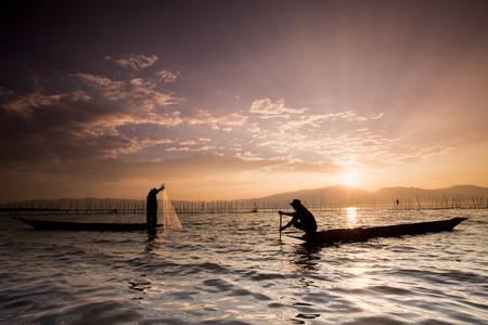 Silhouettes of the traditional fishermen throwing fishing net during sunrise, Thailandの写真素材