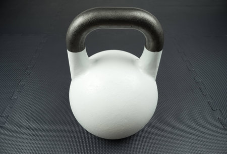 White 10kg competition kettlebell on a fitness studio gym floor with rubber tiles. Potential text space at center of kettlebell.の写真素材