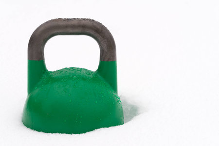 Green weight training kettlebell covered with water droplets outside in the snow. Potential copy space to the right of kettlebell. Green competition kettlebells weigh 24kg.の写真素材