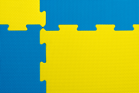 Interlocking blue and yellow foam flooring tiles inside a gym, kindergarten, play room or school classroom. Potential use as a colourful background with copy space.の写真素材