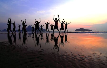 group of happy young people silhouettes jumping on the beach on beautiful summer sunsetの写真素材