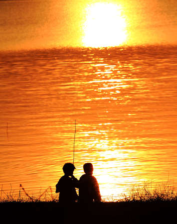 Silhouettes of two children playing along the riverの写真素材