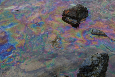 crude oil in sea water and rainbow reflection of crude oil spill on the stone at the beach, focus on crude oilの写真素材
