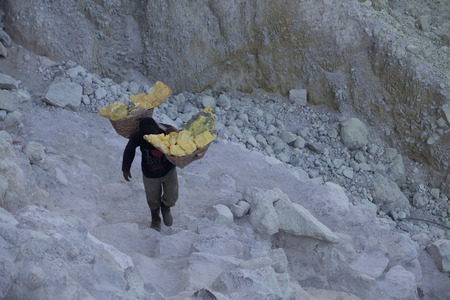 KAWAH IJEN, INDONESIA - OCT 12: Worker carries a basket with pieces of sulfur on his shoulder on October 12, 2015.. Miners each carry up to 90kg of sulfur up steep cliffs at Kawah Ijen volcano.のeditorial素材