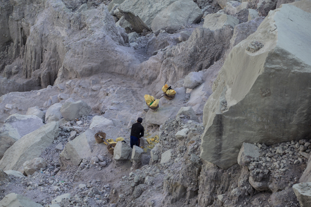 KAWAH IJEN, INDONESIA - OCT 12: Worker carries a basket with pieces of sulfur on his shoulder on October 12, 2015.. Miners each carry up to 90kg of sulfur up steep cliffs at Kawah Ijen volcano.のeditorial素材