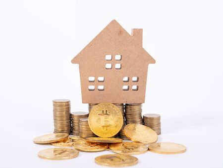 Buying and selling real estate for bitcoins concept with small cottage house and golnden metal bit coin.の写真素材