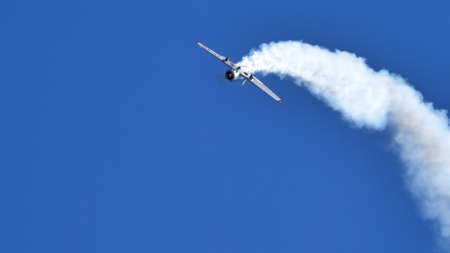 Thiene Italy OCTOBER, 16, 2021 Acrobatic plane upside down with white smoke in blue sky with huge copy space. Yakovlev Yak-52 by YAK Italiaのeditorial素材