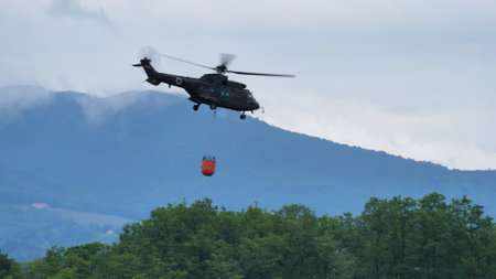 Cerklje Slovenia MAY 29, 2022 Fire helicopter flying over a forest with hanging bucket full of water to drop on the fire. Eurocopter AS532 Cougar Airbus Helicopters of Slovenian Air Force. Copy spaceのeditorial素材
