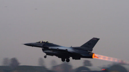 USAF fighter jet ignites its afterburner to full thrust at takeoff, the bright flame contrasting sharply against the grey sky. Ideal for editorial content. Copy space.のeditorial素材