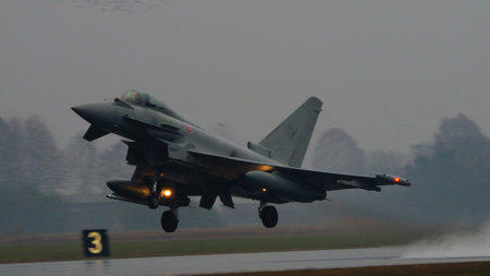 Istrana Italy December 13 2023: Combat aircraft lifts off a flooded runway, casting massive water clouds. Includes copy space. NATO air defense capability in all weather. Copy Space.のeditorial素材