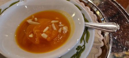 Bowl of creamy pumpkin soup garnished with almond slivers, ready to be enjoyedの写真素材