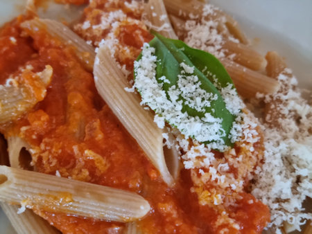 Whole wheat penne pasta topped with a rich tomato sauce, parmesan cheese, and a fresh basil leafの写真素材