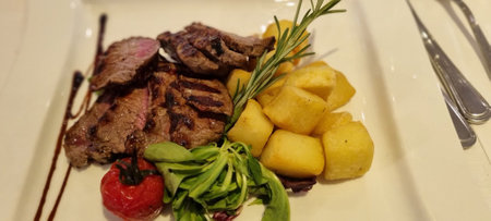 Juicy sliced steak paired with roasted potatoes and fresh greens, plated beautifullyの写真素材