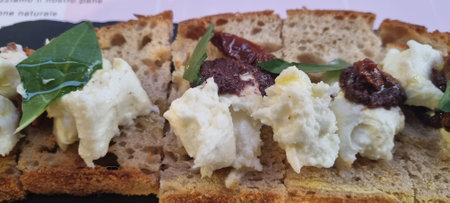 Appetizing close-up of a rustic open sandwich with creamy cheese and sundried tomatoes on grain breadの写真素材