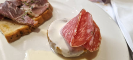 Delicious bruschetta topped with cured meat and cheese, served on a white plateの写真素材