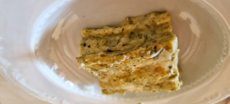 Close-up of a flavorful slice of homemade lasagna seasoned with herbs, served on a white plateの写真素材