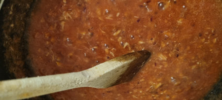 Close-up of a wooden spoon mixing a rich, chunky tomato sauce in a pot