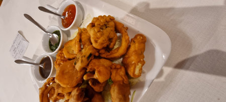 Top view of delicious pakora fritters served with assorted chutneys on a white platterの写真素材