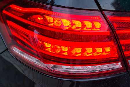 Red tail lights (rear lights, brake lights) of black car close up image.の写真素材