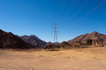 Electric support of high voltage power cables. Metal support with high voltage insulators and against the blue sky in the desert with hills and mountains.の写真素材