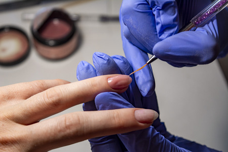 Nail service. Electric nail file drill used in beauty studio. Master of manicure processing operation in blue gloves, debris flying around. Close-up image.の写真素材