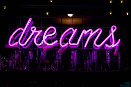 Glowing Purple Neon Inscription DREAMS and glasses on blurred lights background. Dark tones vintage image.の写真素材