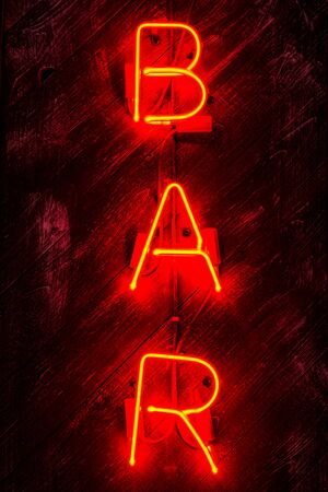 Glowing Neon red  sign BAR on wooden background. Dark tones vintage image.