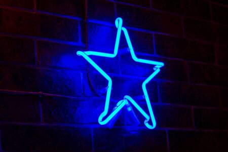 Glowing Neon blue star on dark brick wall background. Dark tones vintage image.の写真素材