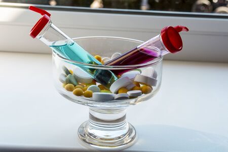 Yellow, white, green tablets and two test tubes with red and blue liquid in a transparent glass vase. The substance is similar to a medicine or vaccine. Theme: healthcare and epidemics of COVID-1)の写真素材