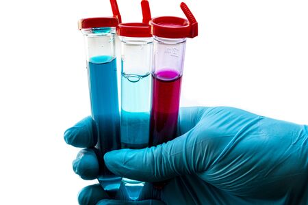 Three test tubes with red and blue liquid in a hand wearing a blue medical rubber glove. The substanceis similar to a medicine or vaccine for the virus. Theme: healthcare and epidemics of COVID-19.の写真素材