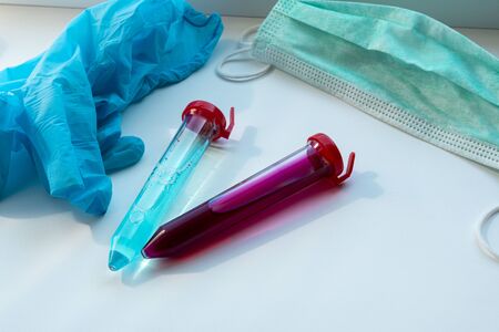 Centrifuge tubes with blue and red substance similar to a medicine or vaccine. medical glove and mask near test tubes. Theme photo: health and epidemics of the coronavirus (COVID-19)の写真素材