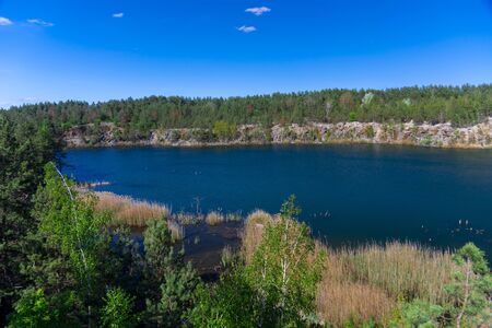Beautiful view of the flooded granite quarry. Shores of granite rocks and forest around the quarry. Landscape panoramic photo.の写真素材
