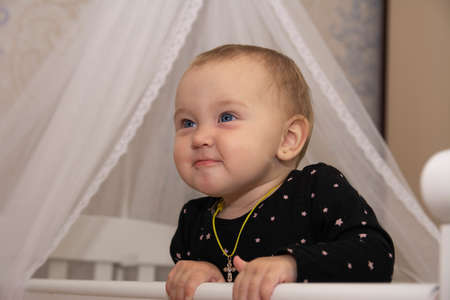 little baby girl peeks out of the white cribの写真素材