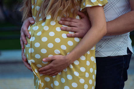 Photo of pregnancy. A pregnant girl in a polka dot dress and her husband hugs her from behind, stroking her belly. Crop photo, part. Pregnancy together.の写真素材