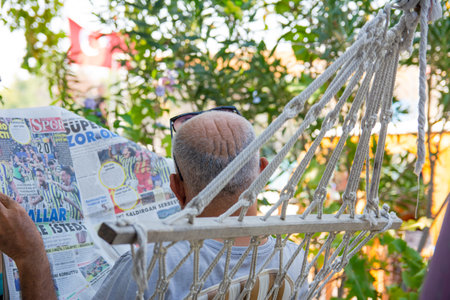 A man reads a newspaper while lying in a hammock in an open-air garden. Rest at nature.のeditorial素材