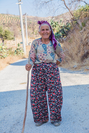 Manavgat, Turkey, 06.09.2022: An old woman poses on the street in a Turkish village. A woman in traditional Turkish clothes smiles on a summer sunny day.のeditorial素材