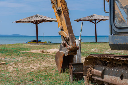 Excavator on the sea beach, against the backdrop of the beach and the sea. The work of the excavator on the sea embankment. Preparing the beach for the holiday season.の写真素材