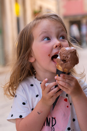 Beautiful Caucasian girl with ice cream on the street of an ancient city in Croatia. A girl enjoys an ice cream summer day on the street among passers-by.の写真素材